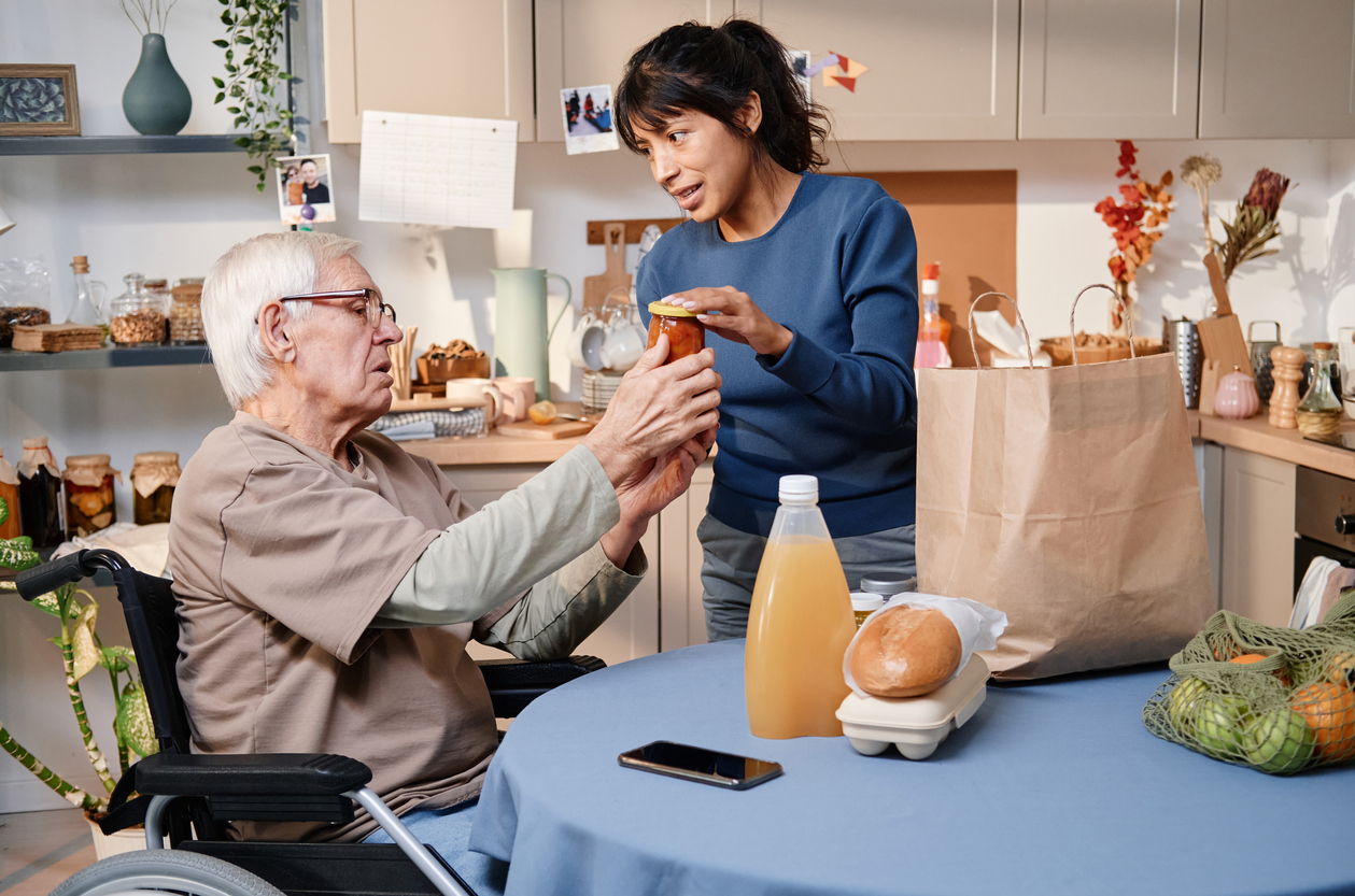 Volunteer delivering food for senior man who using wheelchair, they sitting in the kitchen and discussing food