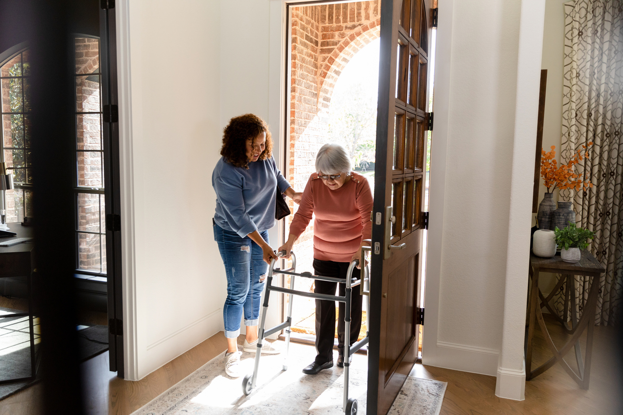 The mid adult woman helps her senior adult friend carefully enter her home.