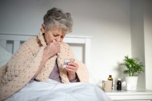 Older woman wrapped in a blanket blowing her nose, showing respiratory symptoms linked to wildfire smoke and poor air quality