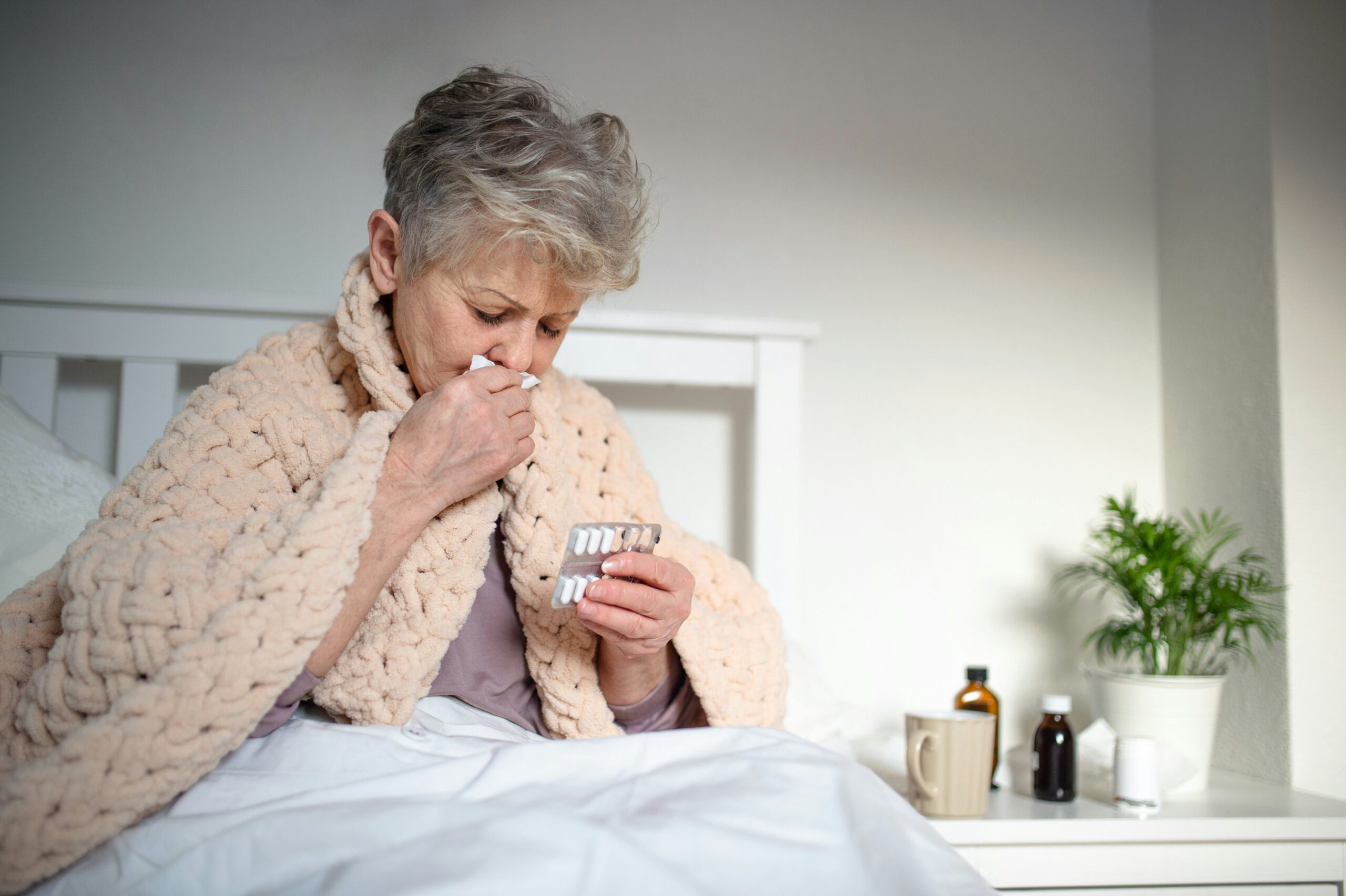 Older woman wrapped in a blanket blowing her nose, showing respiratory symptoms linked to wildfire smoke and poor air quality