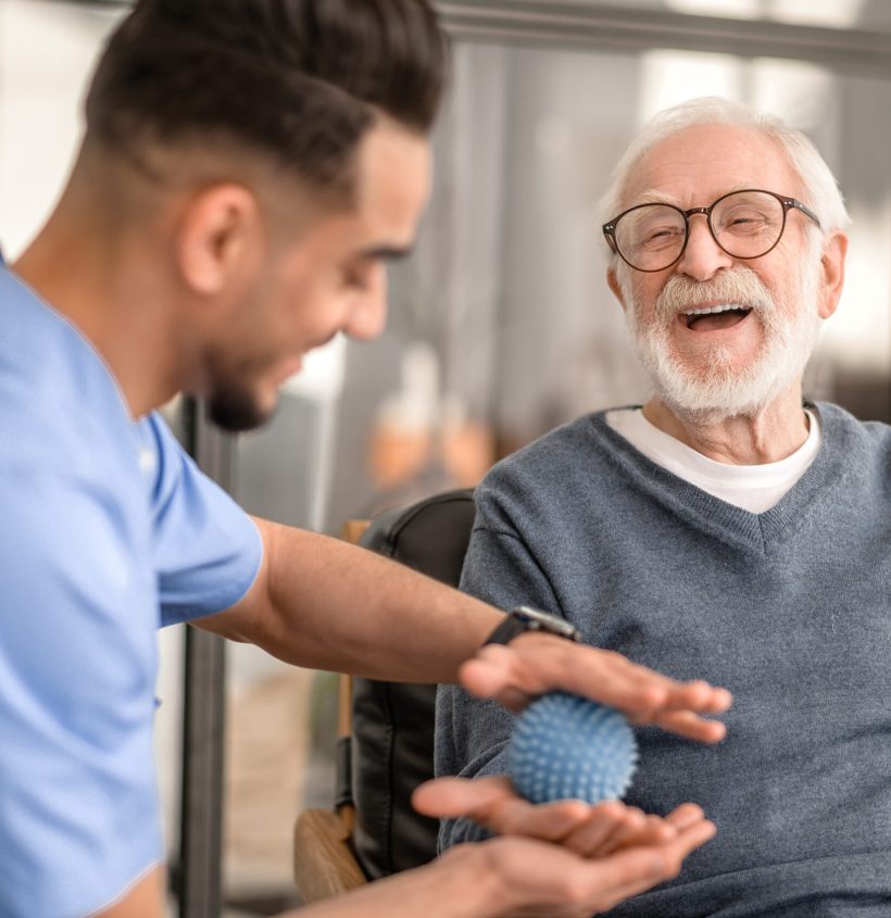 Joyous aged man undergoing a session of physical therapy conducted by an experienced rehabilitation doctor